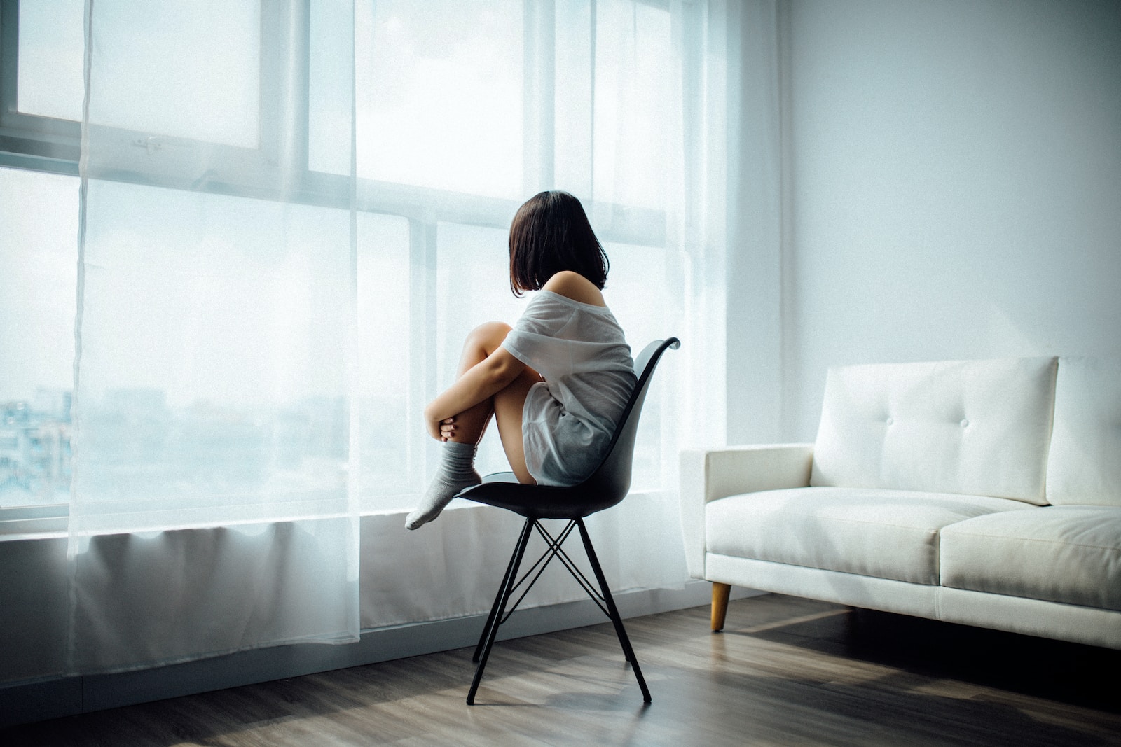 femme assise sur une chaise noire devant une fenêtre à panneaux de verre et rideaux blancs